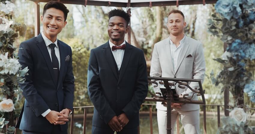 Judge, groomsman, and the groom are all smiling at a wedding