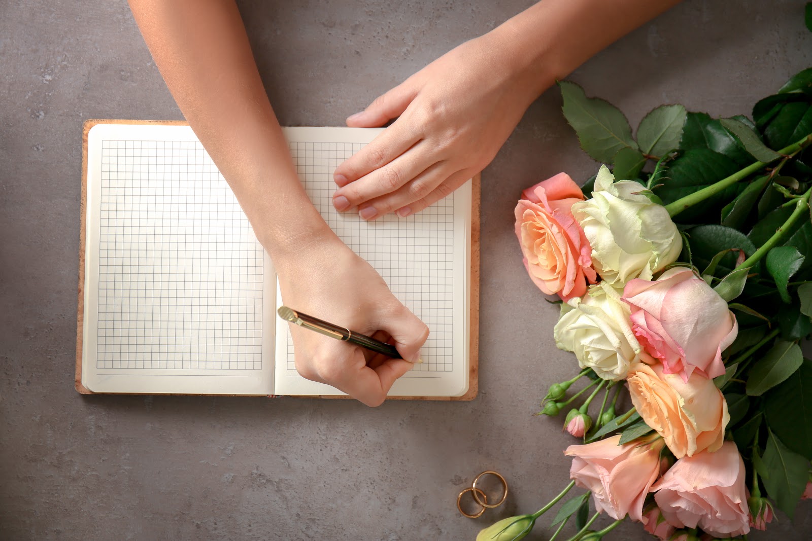 Wedding wishes: Roses and wedding rings next to hands that write notes in a notebook