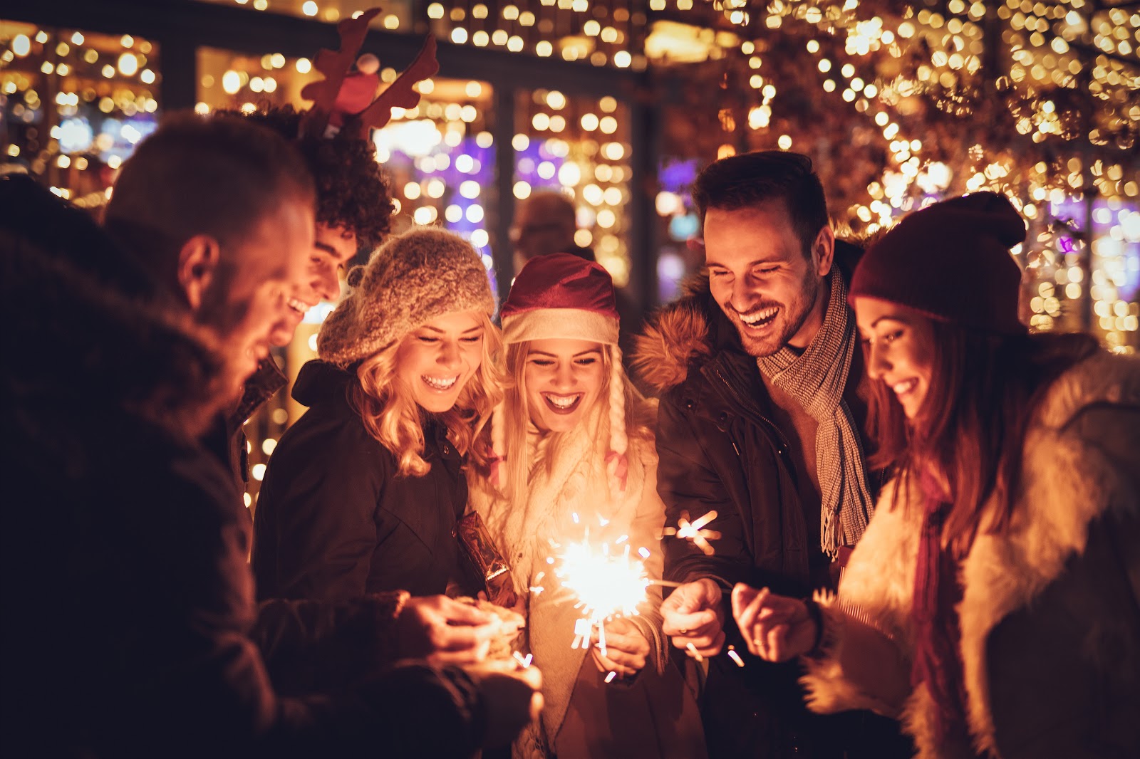 Christmas party ideas: A group celebrates with sparklers and Christmas lights behind them