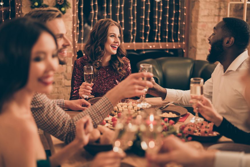 Guests hold up their champagne glasses at a holiday dinner party