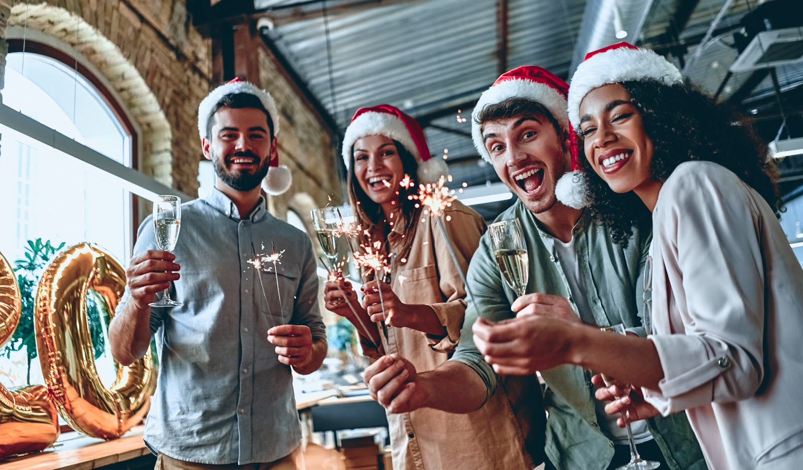 Company Christmas party ideas: A group of coworkers hold champagne glasses at an office holiday party