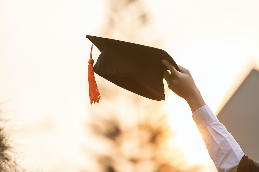 A hand holds a graduation cap in the air