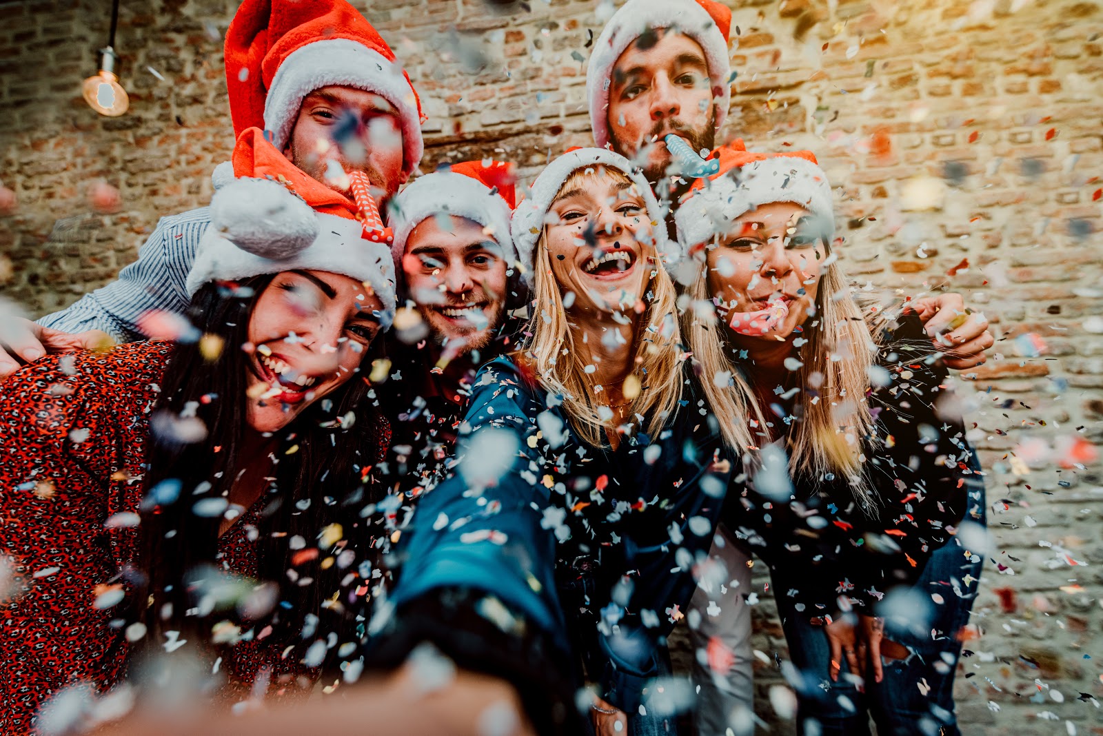 text message invitations: Group of friends wearing Santa hats taking a photo while surrounded by confetti