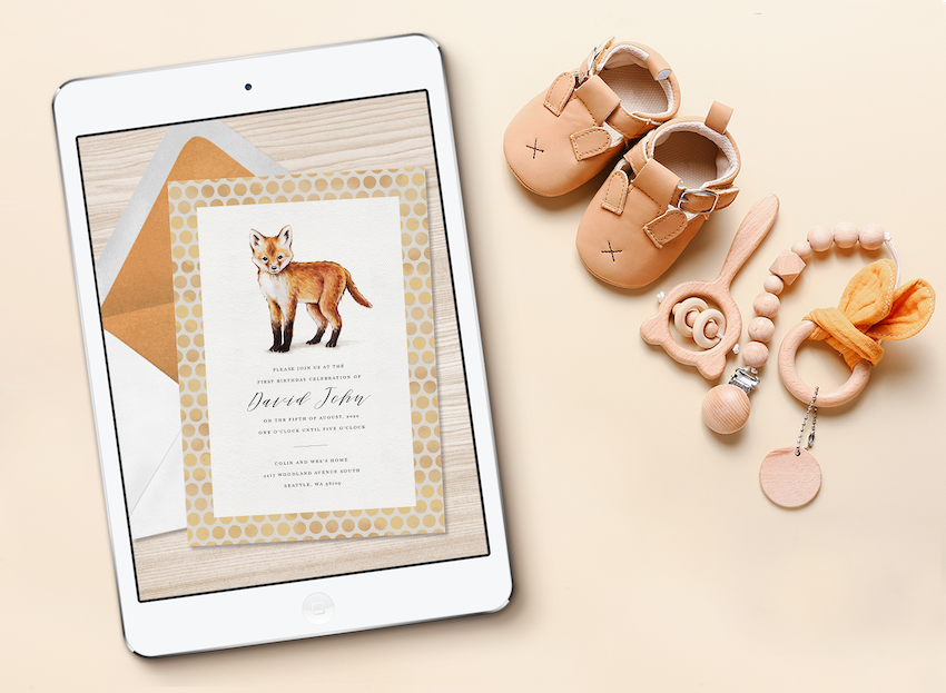 An online baby shower invitation displayed on a tablet screen, next to baby shoes and toys