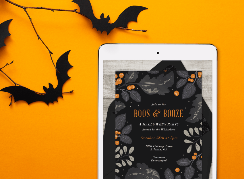 A digital halloween invitation on a tablet, surrounded by die-cut paper bats