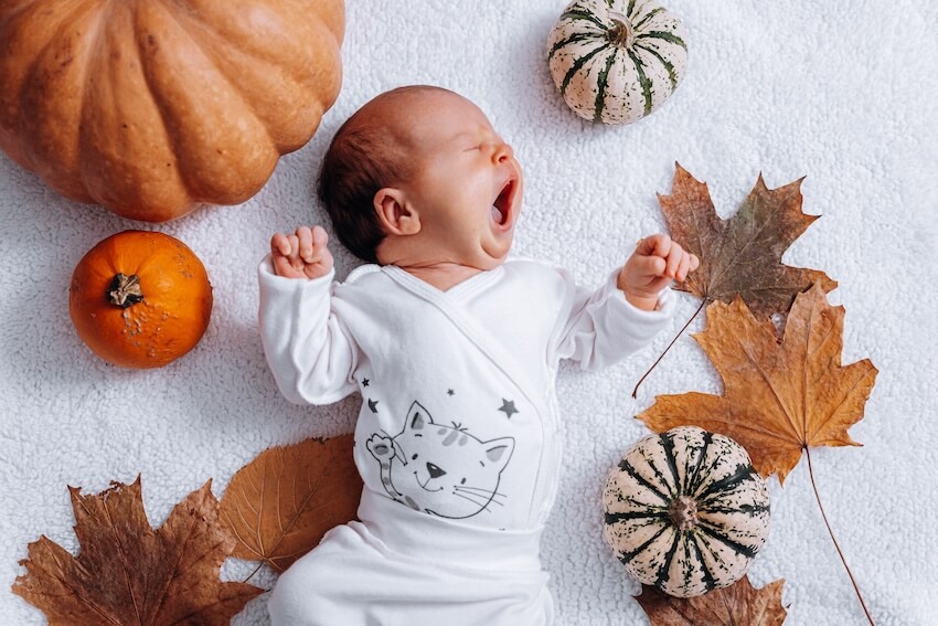 Pumpkin baby shower invitations: a yawning baby surrounded by pumpkins and autumn leaves