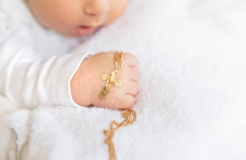 What to write in a baptism card: baby's hand holding a golden cross necklace