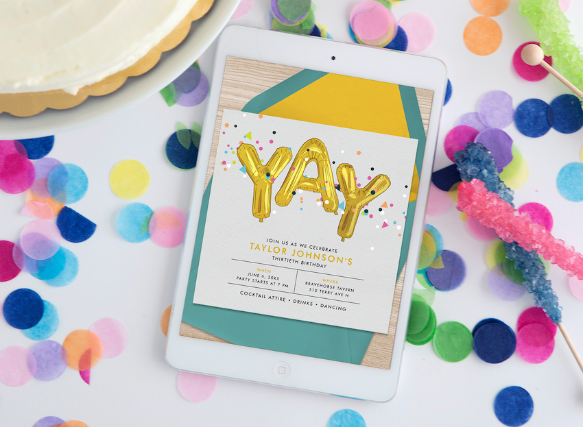 A tablet, surrounded by confetti and party decor, displays birthday invitations online