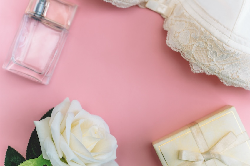 Lingerie shower invitations: bottle of perfume, a white rose, a small gift, and a lingerie on a pink background