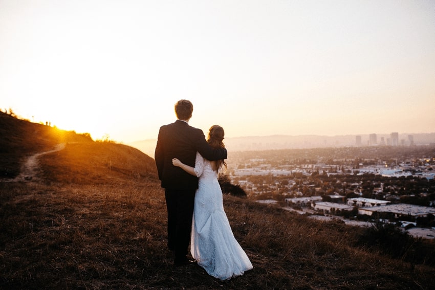 When to send wedding invitations: bride and groom side hugging on top of a hill