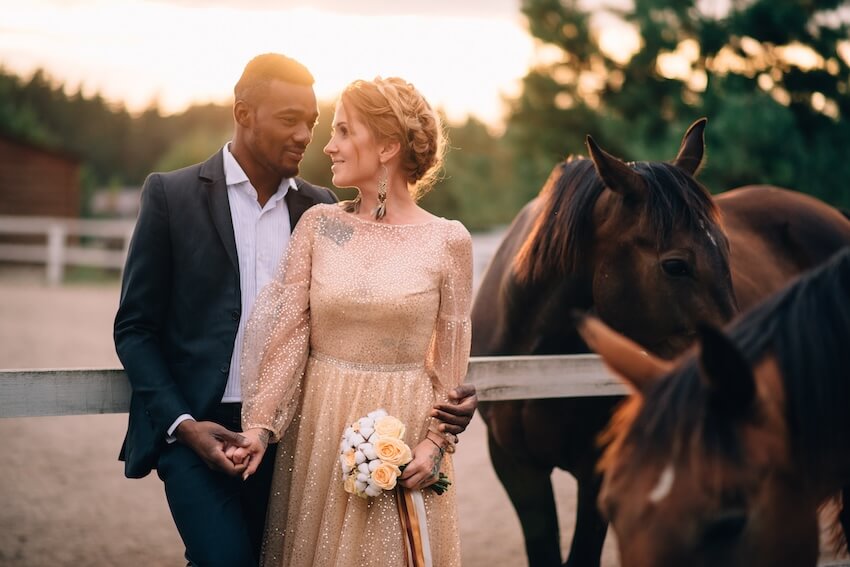When to send wedding invitations: bride and groom standing beside 2 horses