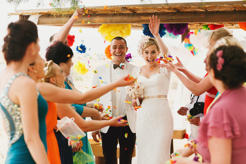 Rainbow wedding theme: bride and groom walking while guests throw confetti