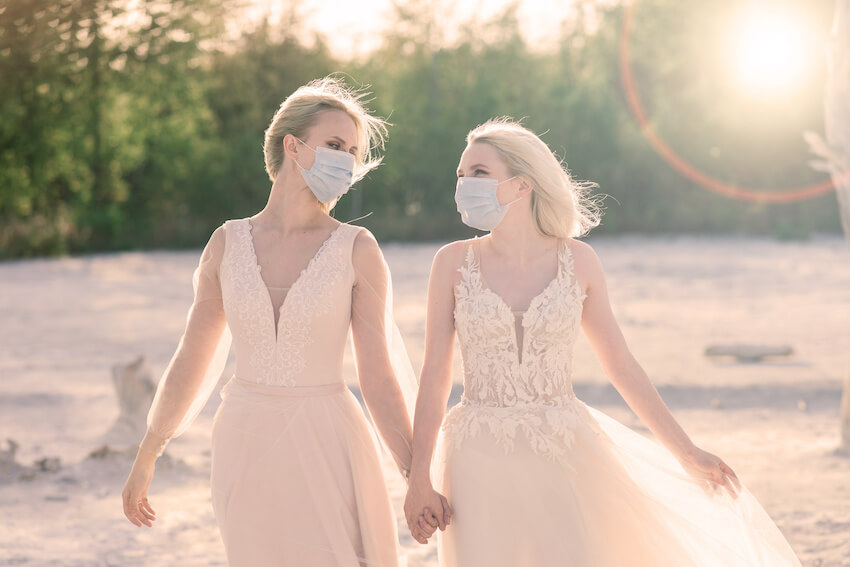 Planning a wedding during COVID: couple wearing masks and holding hands while walking on the beach
