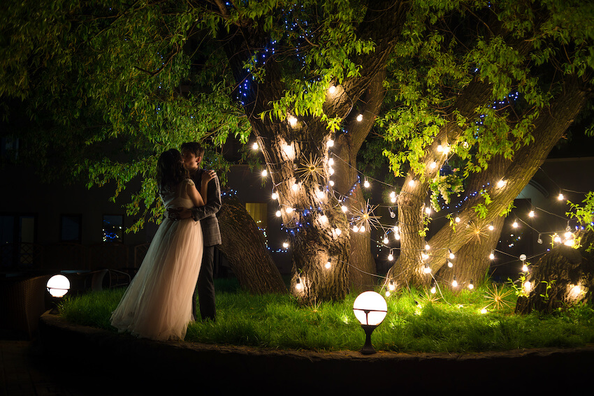 Whimsical wedding: bride and groom kissing under a tree with lights