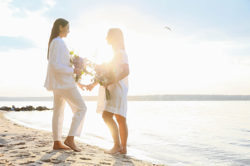 Couple holding flowers while standing on the beach