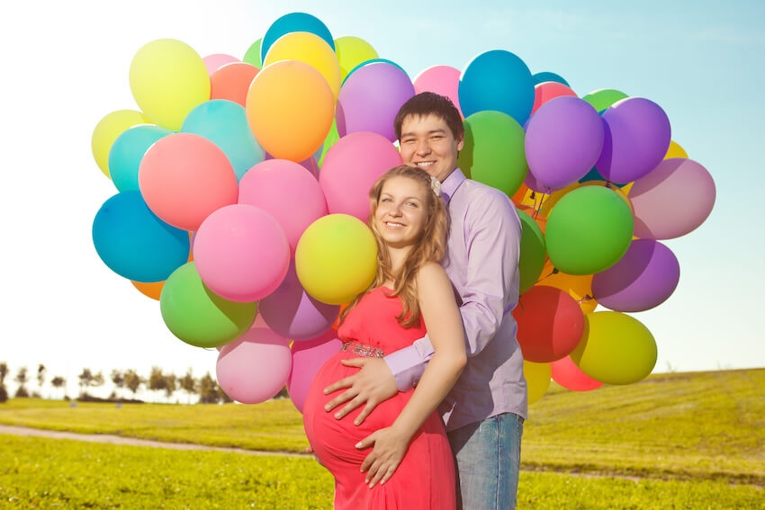 Rainbow baby announcement: couple smiling at the camera with balloons in the background