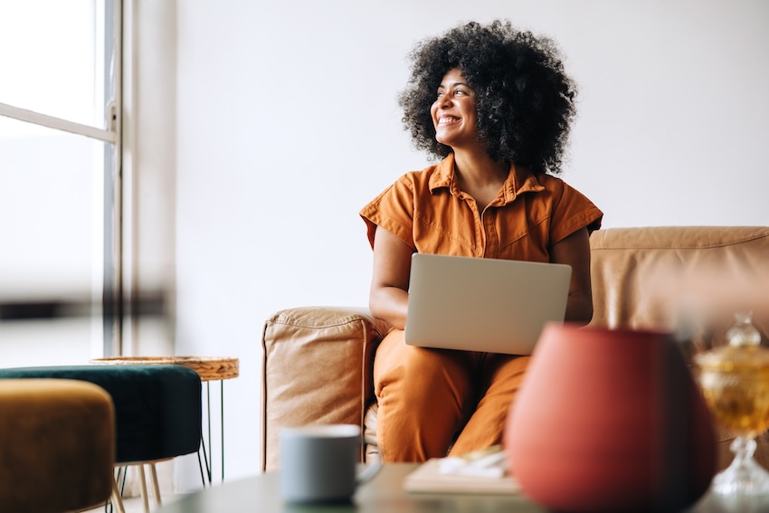Thinking of you messages: curly-haired woman happily looking out the window while using her laptop