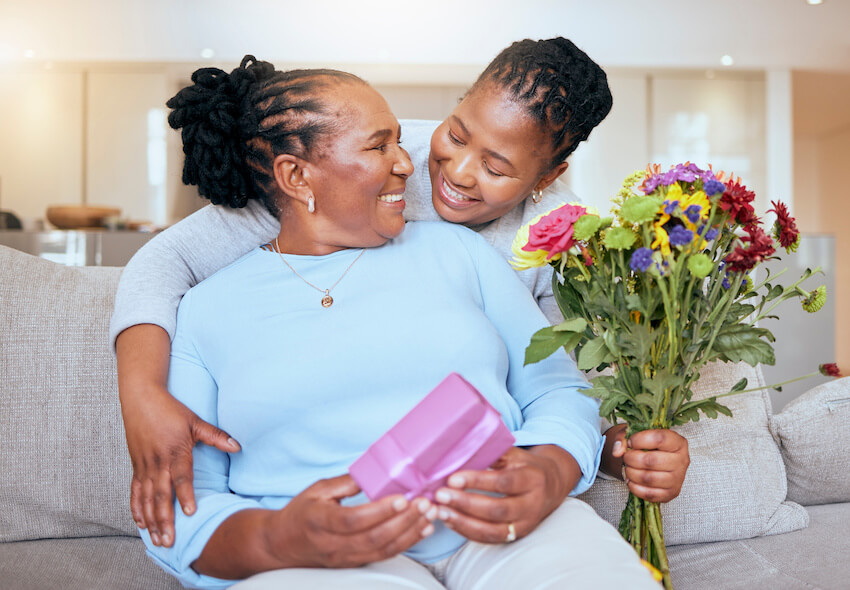 Happy birthday beautiful lady: daughter hugging her mother while handing her a bouquet