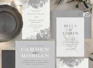 Three elegant wedding invitations laid out with greenery and fine china