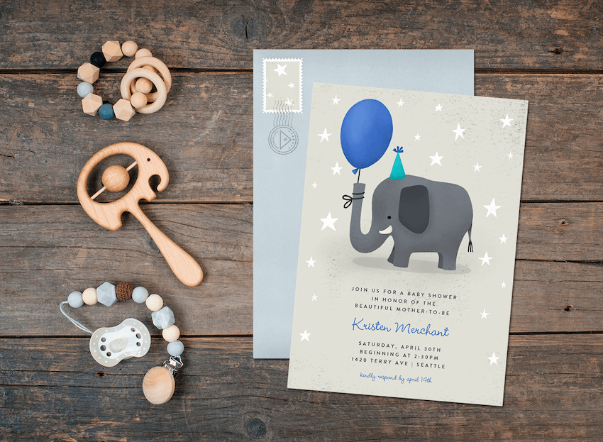 An elephant baby shower invitation on a wood table with envelope and baby toys