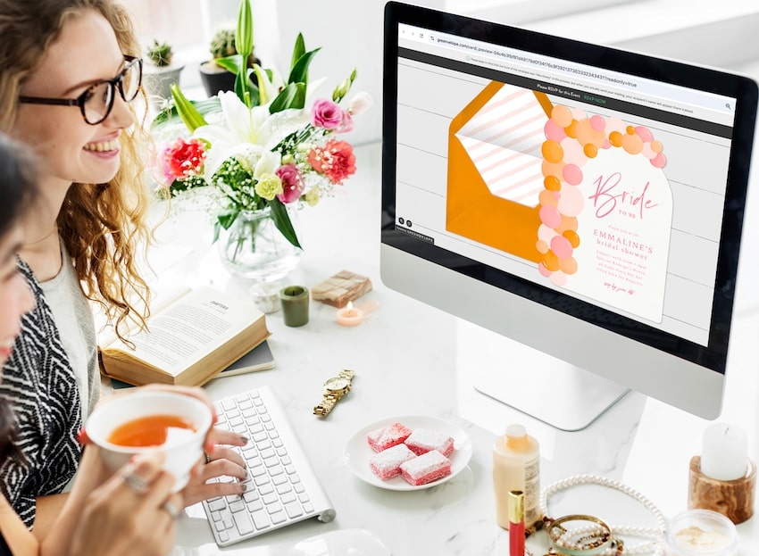 How to plan a bridal shower: friends looking at a bridal shower invitation on a computer screen