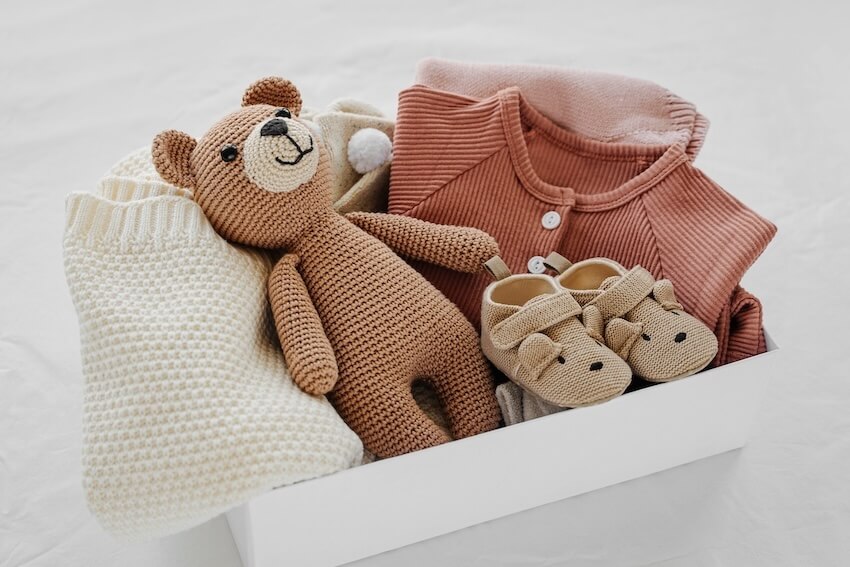 Gift box with a teddy bear, a pair of baby shoes, and some baby clothes