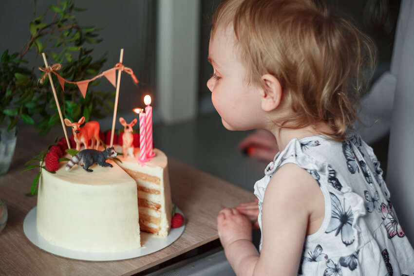 3rd birthday party themes: girl blowing out candles on a birthday cake