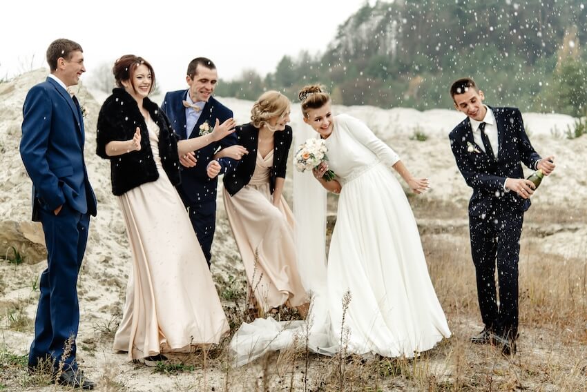 Groom and bride with their guests popping a bottle of champagne