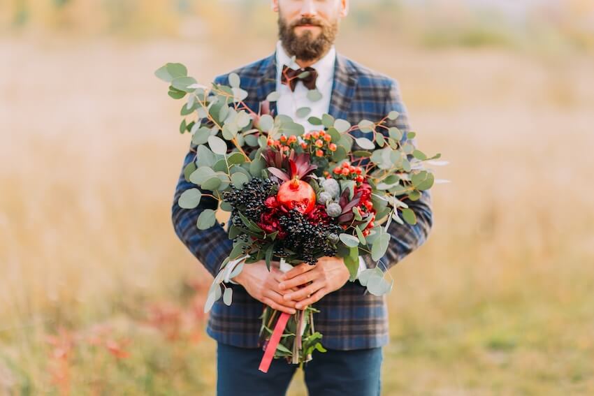 Fall wedding colors: groom carrying a bouquet of fruits with leaves