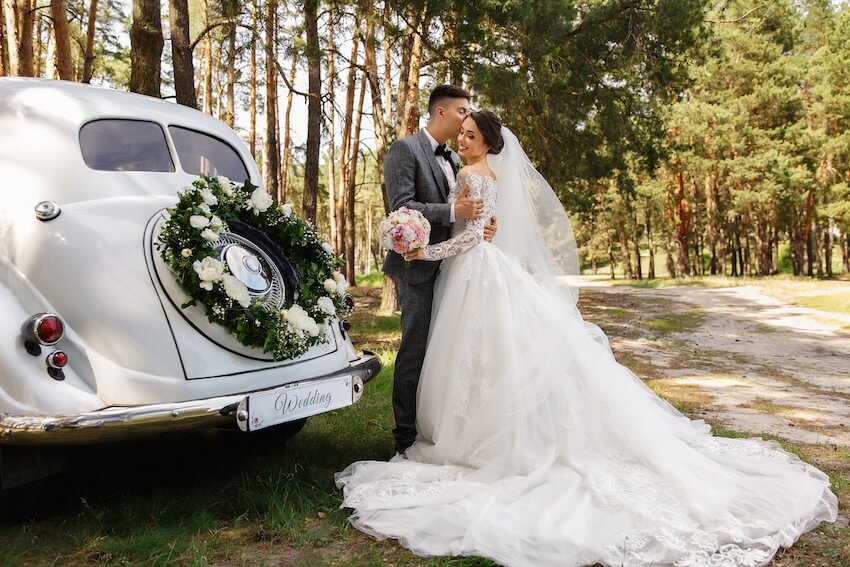 Wedding styles: groom kissing his bride beside a classic wedding car