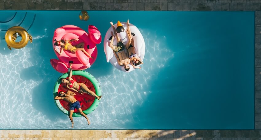 Bring your own pool party: group of friends lying on colorful floaties in a pool