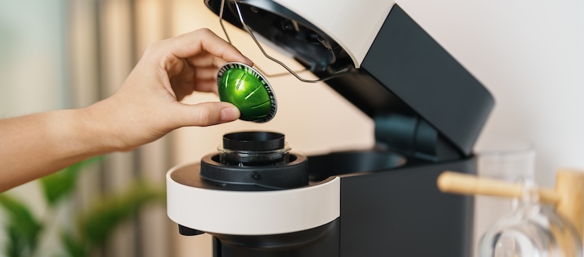 21st birthday gift ideas: hand placing a green coffee capsule into a coffee machine