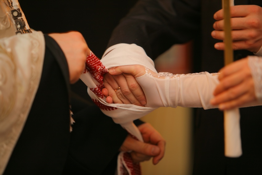 Priest using a piece of cloth to tie a couple's hands together