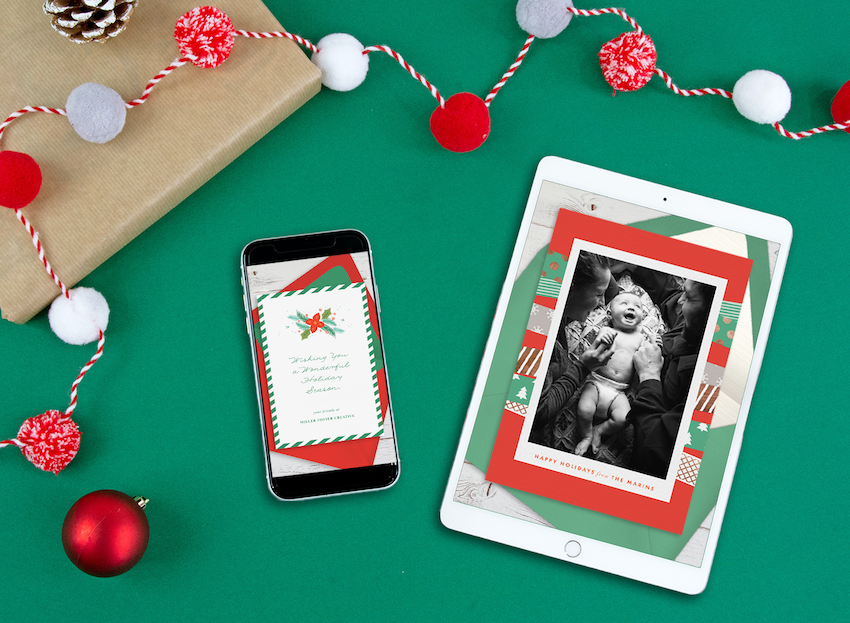 Digital holiday cards displayed on a tablet and phone, surrounded by garland