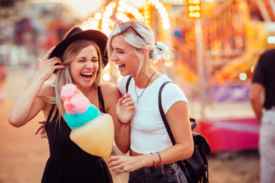 carnival theme party: Two young women laughing together in a carnival while one holds a cotton candy