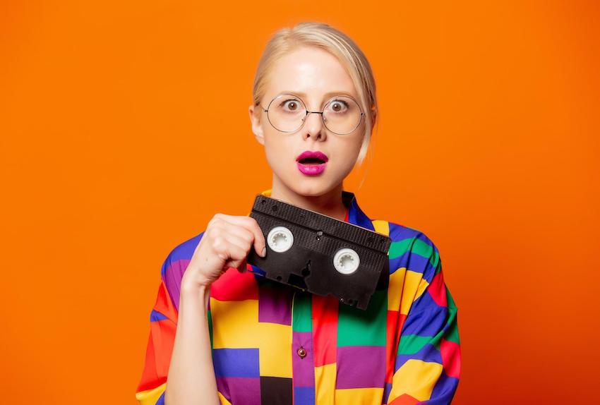 Woman wearing 90s shirt and glasses holding VHS tape