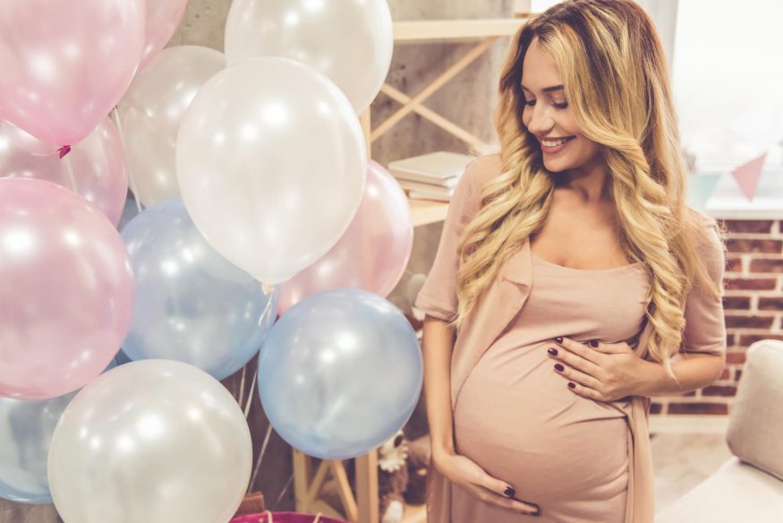 virtual baby shower ideas: Pregnant woman smiling and looking at the balloons
