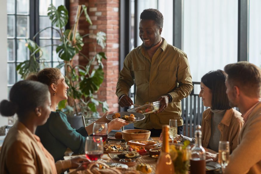 dinner party games for adults: Man serving food while hosting a dinner party for his friends