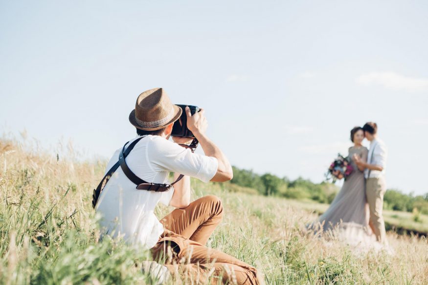 questions to ask wedding photographer: Photographer taking pictures of the bride and groom in a field