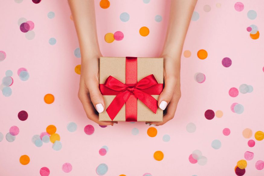 birthday gifts during quarantine: Woman holding a gift against a pink background with polka dots