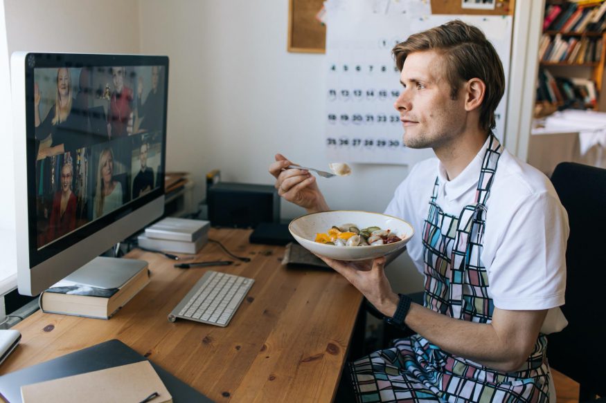 Man wearing an apron while eating in front of his computer