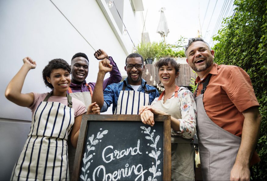 grand opening invitation: Smiling workers with a grand opening sign