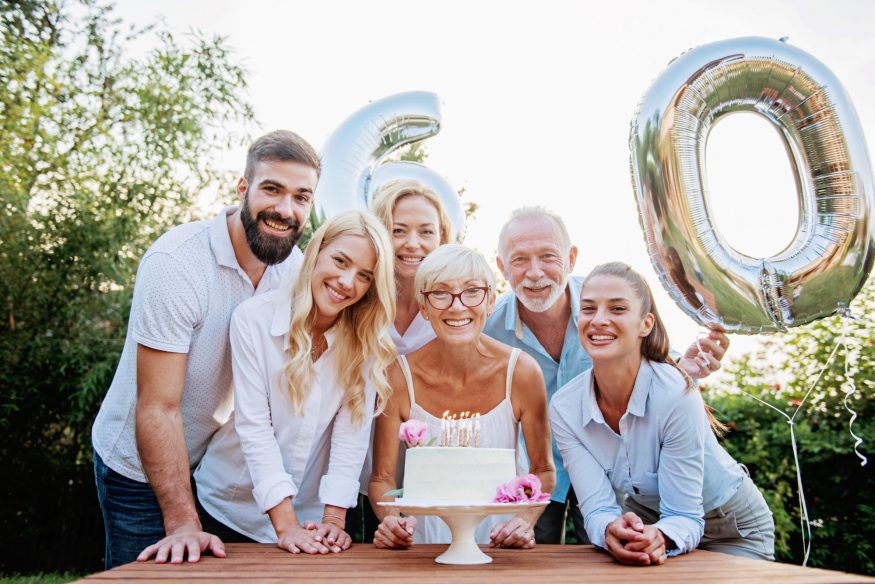 60th birthday party ideas: Woman smiling behind her cake while surrounded by her family