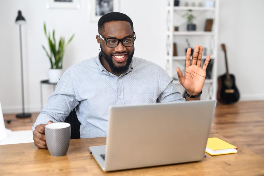 remote team building activities: Man smiling and waving in front of his laptop