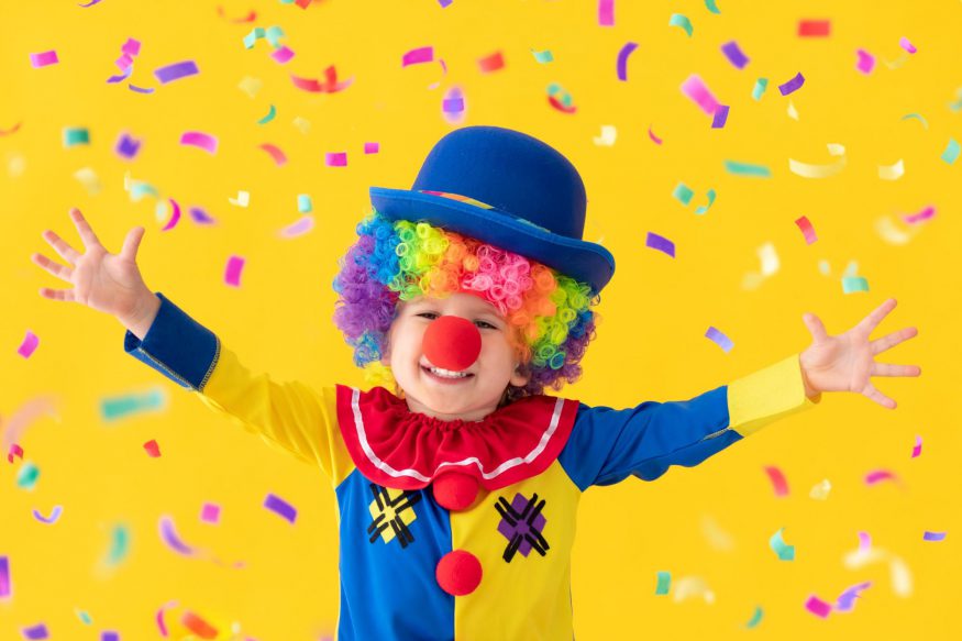 carnival theme party: Child in clown costume against a yellow background with confetti floating around