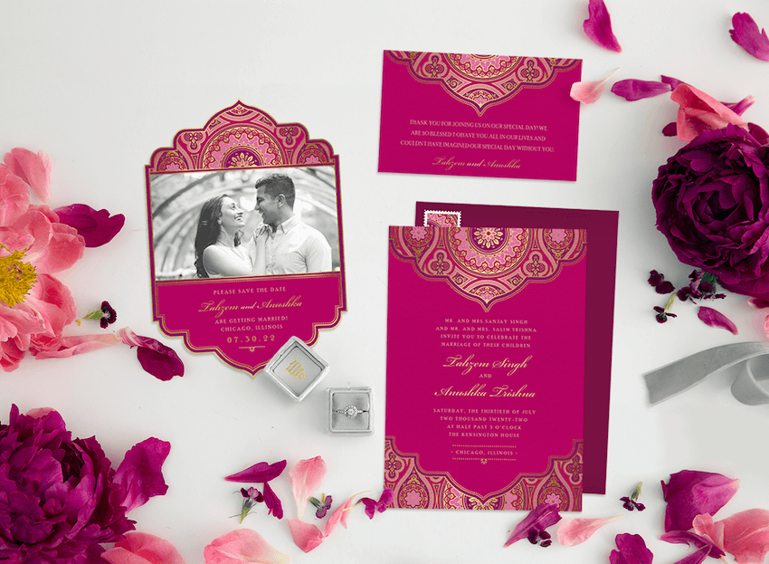 Three Indian wedding invitations laid out on a white table with fuchsia flowers