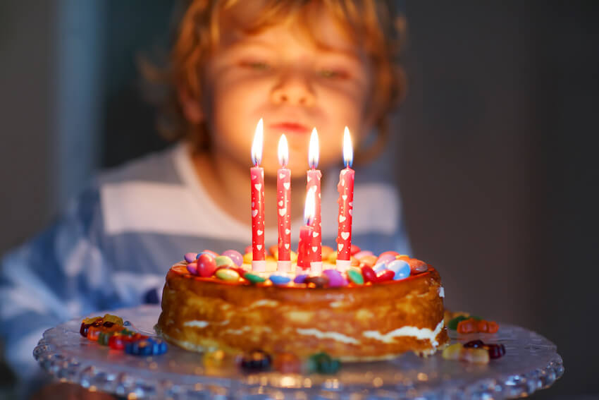 Toddler birthday party ideas: kid blowing out 4 birthday candles on a cake