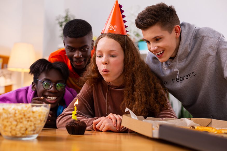 teen birthday party ideas: girl blowing out candle while surrounded by friends at a party