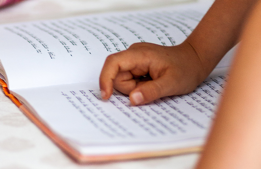 A child's hand points to the Torah