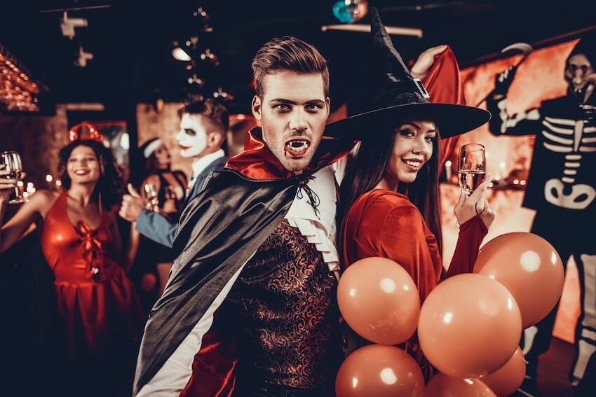 Man and woman dressed as a vampire and a witch, posing for a picture at a Halloween party